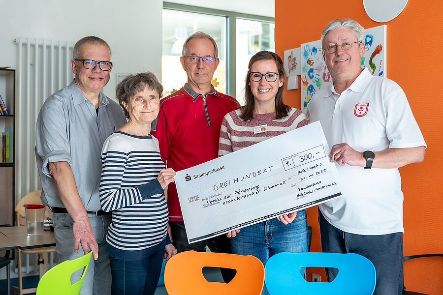 Fünf Personen stehen im Aufenthaltsraum einer Kinderstation eines Krankenhauses und halten einen Spendenscheck in den Händen.  Fünf Personen stehen im Aufenthaltsraum einer Kinderstation eines Krankenhauses und halten einen Spendenscheck in den Händen.