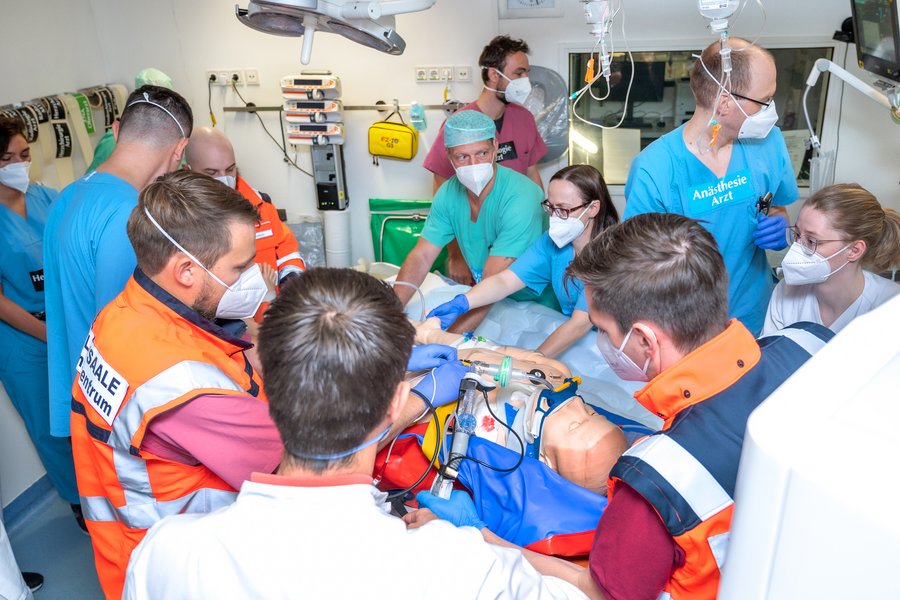 Mitarbeitende der Universitätsmedizin Halle führen eine Übung im Schockraum durch. Viele Menschen stehen um die Simulationspuppe herum und erledigen verschiedene Aufgaben.  Mitarbeitende der Universitätsmedizin Halle führen eine Übung im Schockraum durch. Viele Menschen stehen um die Simulationspuppe herum und erledigen verschiedene Aufgaben.