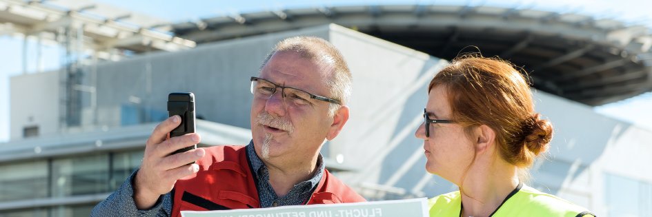 Zwei Menschen im Freien auf einer Baustellen mit Plänen im Gespräch