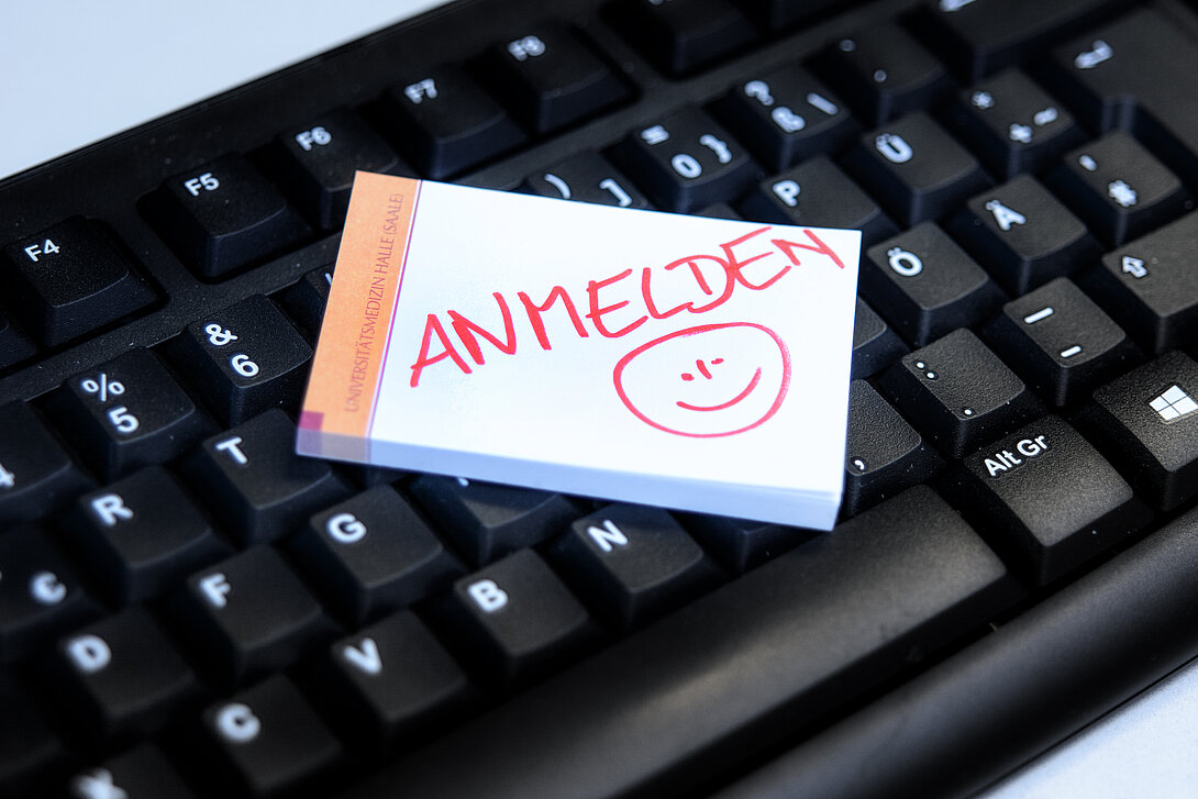 Zettel mit dem Wort Anmelden liegt auf einer schwarzen Tastatur