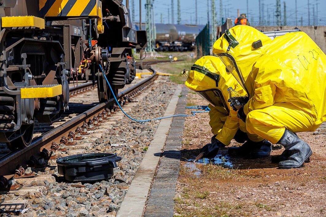 Eine Person in einem Schutzanzug kniet neben einem Gleis aus einem Bahngelände.