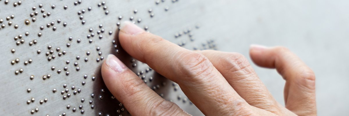 Finger lesen einen Text in Brailleschrift auf einer Info-Tafel.