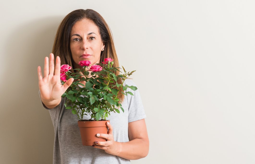 Eine Frau hält einen Blumentopf vor ihrem Körper und zeigt mit der Hand das Stopp-Zeichen - Symbol für kein Blumentopf