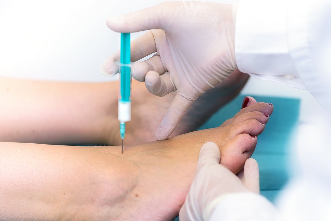 Medizinisches Personal setzt eine Spritze am Fuß einer Patientin an