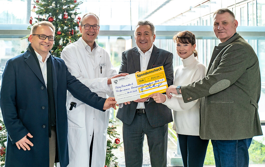 Fünf Personen halten einen Spendenscheck über 500 Euro in den Händen. Die zweite Person von links trägt einen Arztkittel.