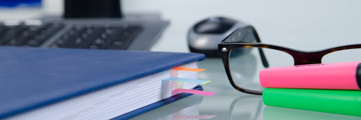 Kalenderbuch mit bunten Schnipseln, daneben Brille, Mouse und Tastatur