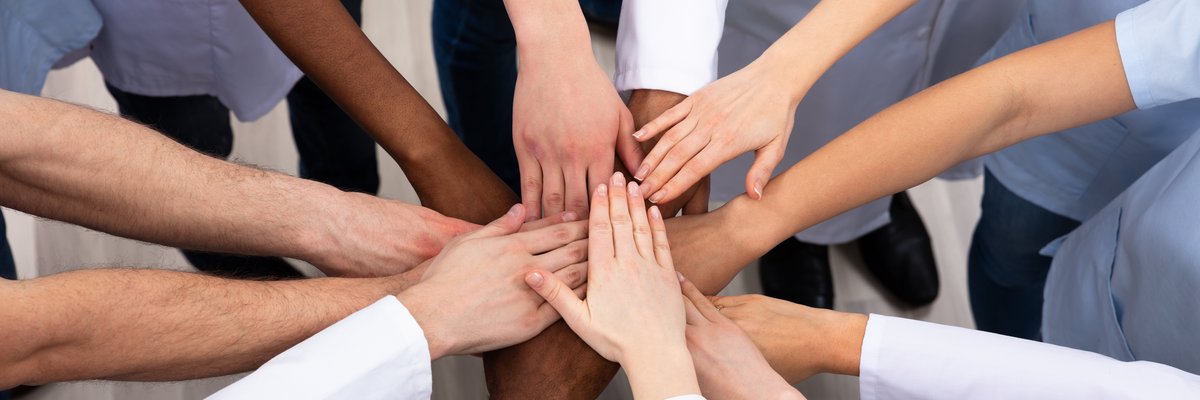 Menschen strecken ihre Arme im Kreis stehend zur Mitte als Sinnbild für Team