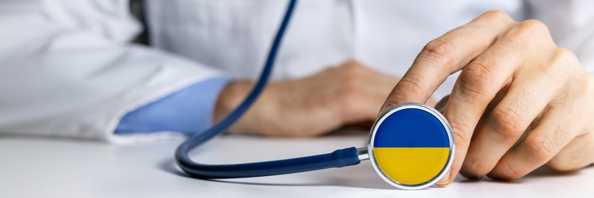 Mensch in weißen Kittel mit Stetoskop, dessen Abhörteil in blau-gelb ist