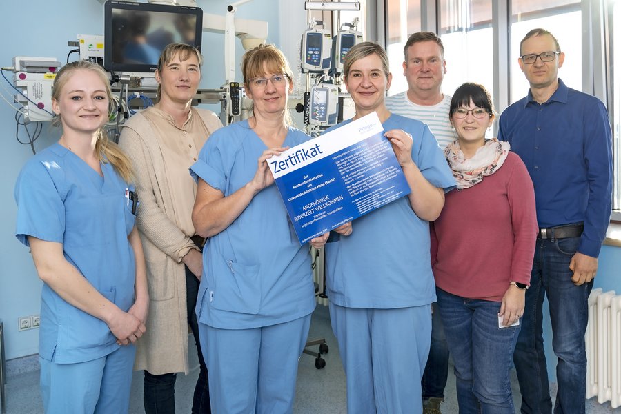 Mitarbeitende der Abteilung für Neonatologie und Pädiatrische Intensivmedizin der Universitätsmedizin Halle stehen in einem Zimmer auf Station. Zwei Mitarbeiterinnen halten ein Zertifikat in den Händen.  Mitarbeitende der Abteilung für Neonatologie und Pädiatrische Intensivmedizin der Universitätsmedizin Halle stehen in einem Zimmer auf Station. Zwei Mitarbeiterinnen halten ein Zertifikat in den Händen.