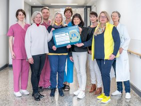 Eine Gruppe von Menschen steht in einem Klinikflur. Drei Personen halten einen symbolischen Spendenscheck in den Händen.