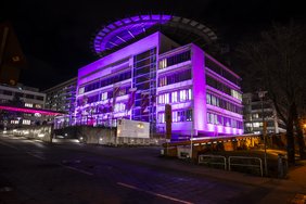 Das Hauptgebäude des Universitätsklinikums im Dunklen mit lila Beleuchtung.