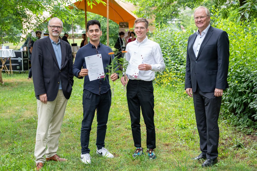 Vier Männer, zwei davon mit Urkunden und Blumen stehen auf einer Wiese nebeneinander. Im Hintergrund sind Menschen in einem Zelt sowie Büsche und Bäume zu sehen  Vier Männer, zwei davon mit Urkunden und Blumen stehen auf einer Wiese nebeneinander. Im Hintergrund sind Menschen in einem Zelt sowie Büsche und Bäume zu sehen