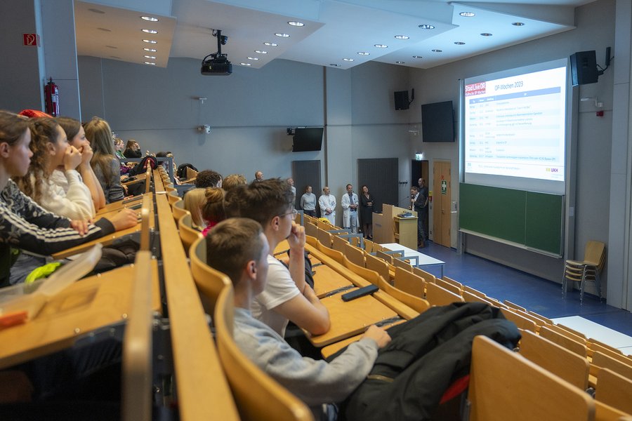 Ein Hörsaal voller Studierender, die auf eine großformatige Präsentation blicken.   Ein Hörsaal voller Studierender, die auf eine großformatige Präsentation blicken. 