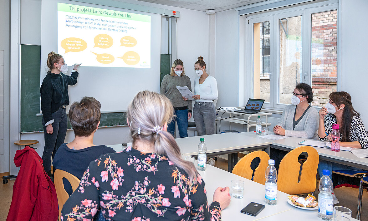 Mehrere Menschen bei einer Tagung, sitzend am Tisch oder an der Tafel für eine Präsentation