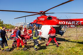 Rettungsteams transportieren eine verletzte Person auf einer Trage zu einem Rettungshubschrauber.