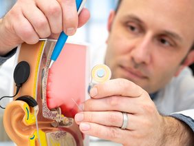 Ein Mann zeigt mit einem blauen Kugelschreiber an einem Modell ein Cochlea-Implantat nach Einsetzen im Ohr.