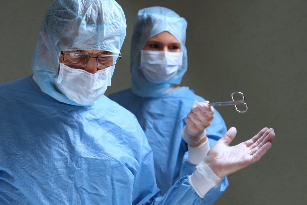 Eine Frau in blauer OP-Kleidung reicht einem Mann in blauer OP-Kleidung ein medizisches Gerät für eine OP