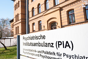 Ansicht einer Hausfassade aus Klinker. Im Vordergrund ist ein Schild der Psychiatrischen Institutsambulanz zu sehen.