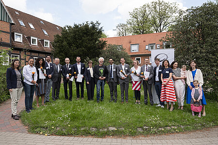19 Personen stehen in einer Reihe auf einer Wiese für ein Gruppenfoto vor den in die Marie-Christian-Heimen in Kiel.