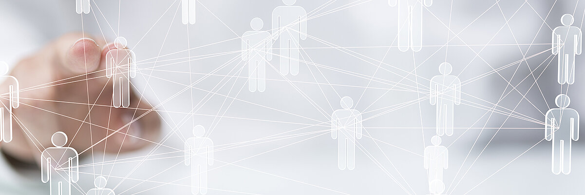 Eine Hand tippt auf Figuren auf einer durchsichtigen Tafel. Die Figuren sind miteinander vernetzt.