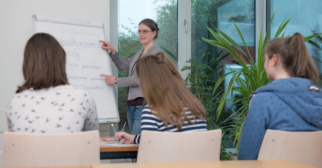 Frau am Flipchart erkärt drei Zuhörerinnen etwas über Sozialkompetenz