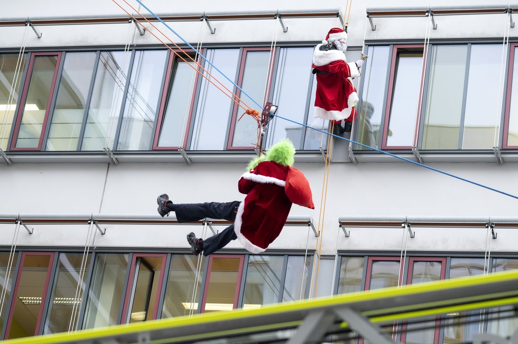 Als Grinch und Weihnachtsmann verkleidete Feuerwehrleute seilen sich vom Gebäude des Universitätsklinikums Halle (Saale) ab.