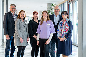 Gruppenbild: Vier Organisator:innen des Geriatrietags 2026 der Universitätsmedizin Halle, die Dekanin der Medizinischen Fakultät der MLU und die Keynote-Speakerin stehen in einem Gang. 