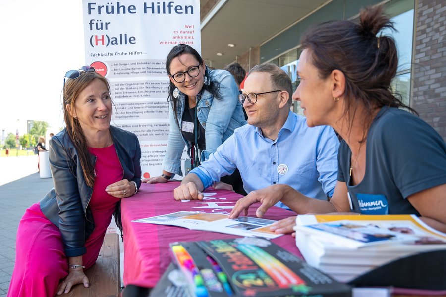 Halles Amtsärztin Christine Gröger und die Koordinatorin der Frühen Hilfen in Halle Julia Franke im Gespräch mit Prof. Dr. Roland Haase und Hebamme Katja Schumann. Sie sitzen an einem Tisch, auf dem ein rotes Banner mit UMH-Logo liegt. Im Hintergrund sieht man ein Roll-up von den Frühen Hilfen Halle.  Halles Amtsärztin Christine Gröger und die Koordinatorin der Frühen Hilfen in Halle Julia Franke im Gespräch mit Prof. Dr. Roland Haase und Hebamme Katja Schumann. Sie sitzen an einem Tisch, auf dem ein rotes Banner mit UMH-Logo liegt. Im Hintergrund sieht man ein Roll-up von den Frühen Hilfen Halle.