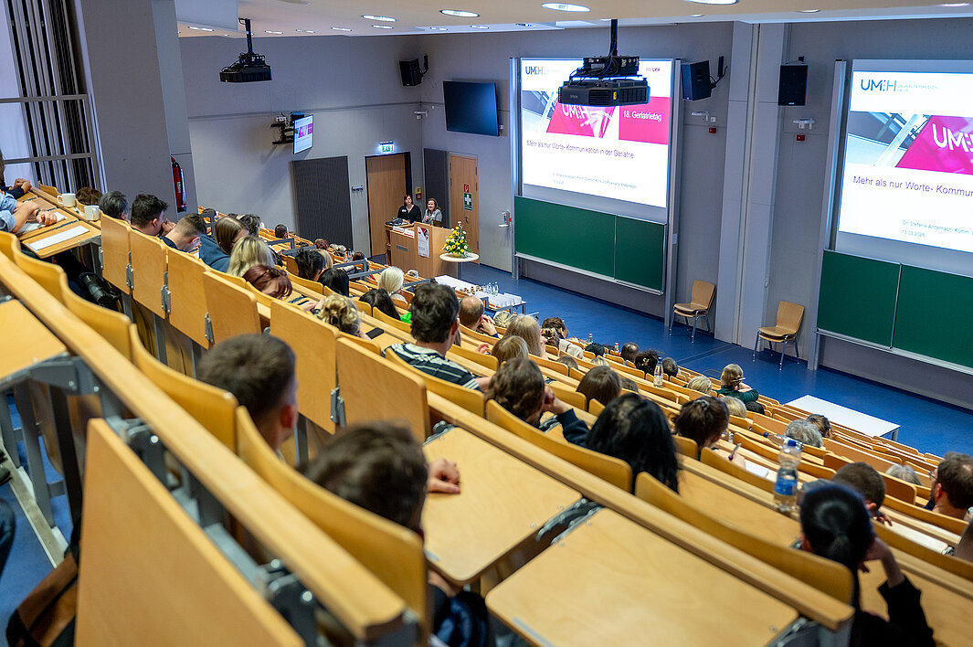 Teilnehmende des Geriatrietags 2026 sitzen in einem Hörsaal der Universitätsmedizin Halle. Vorn spricht eine Person ins Mikrofon, eine weitere Person steht daneben.
