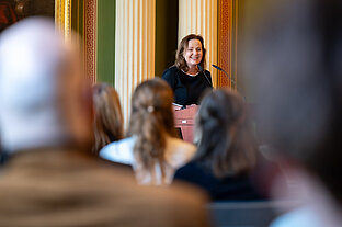 Blick aus dem Publikum auf Prof. Dr. Heike Kielstein, die an einem Rednerpult steht und freundlich blickt.