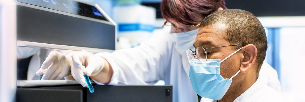 Ein Laborant und eine Laborantin schauen sich eine blaue Flüssigkeit in einem Reagenzglas an