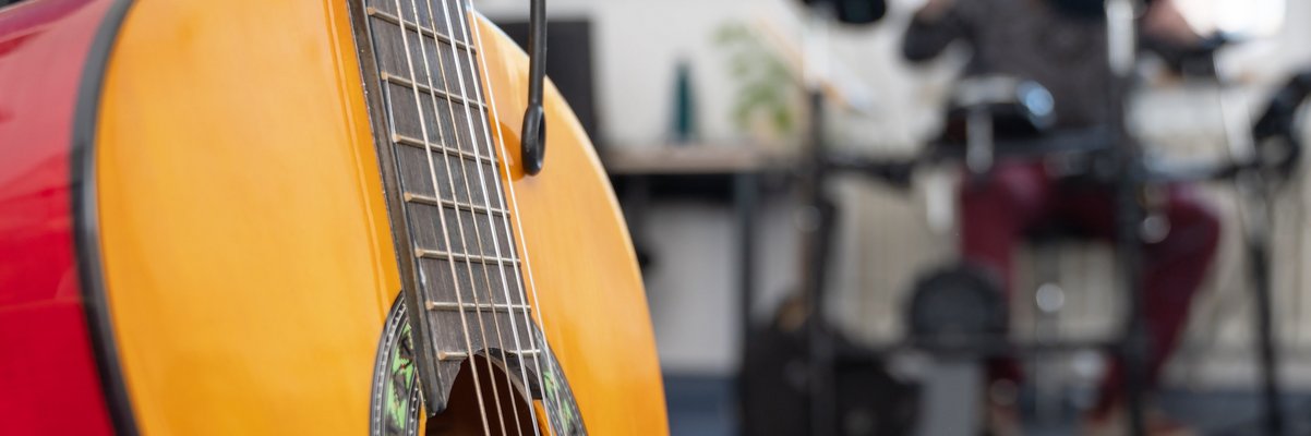 Gitarre im Vordergrund, Menschen musizieren