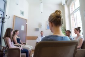 Eine Gruppe von Menschen sitzt in einem Raum auf Stühlen im Kreis