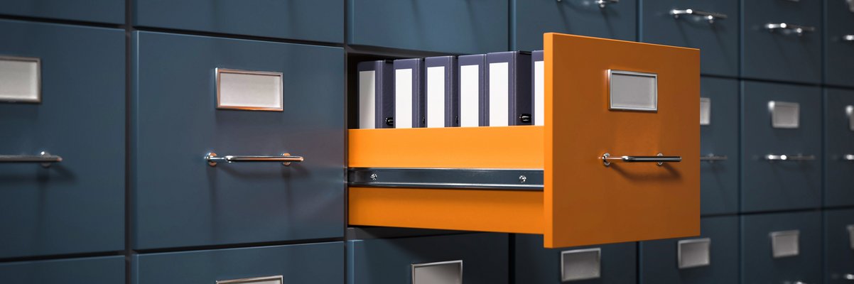 Grauer Aktenschrank, ein Fach in Orange ist herausgezogen. Dort sind Akten zu sehen.