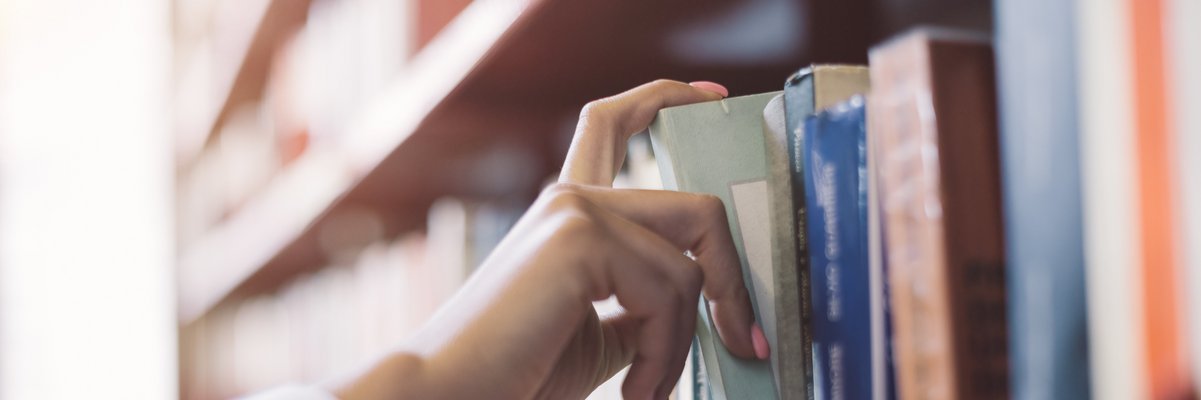 Ein Mensch nimmt ein Buch aus einem Bücherregal, ist es eine Hand zu sehen