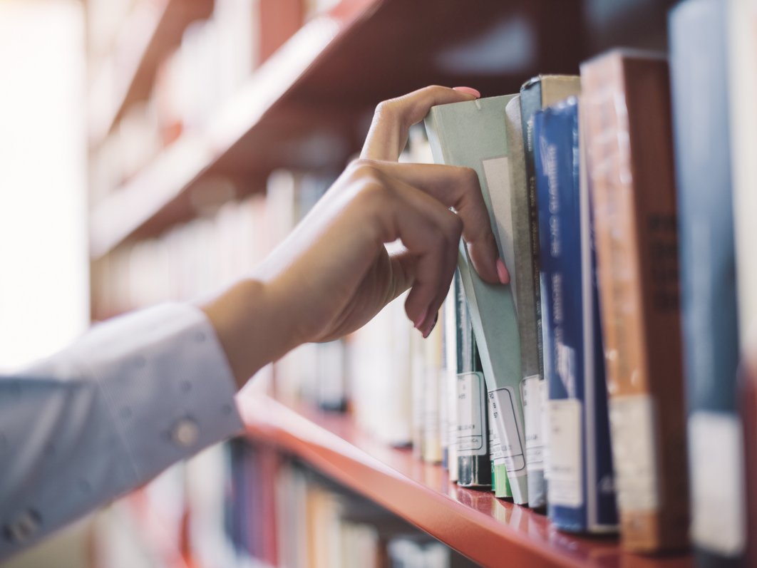 Ein Mensch nimmt ein Buch aus einem Bücherregal, ist es eine Hand zu sehen