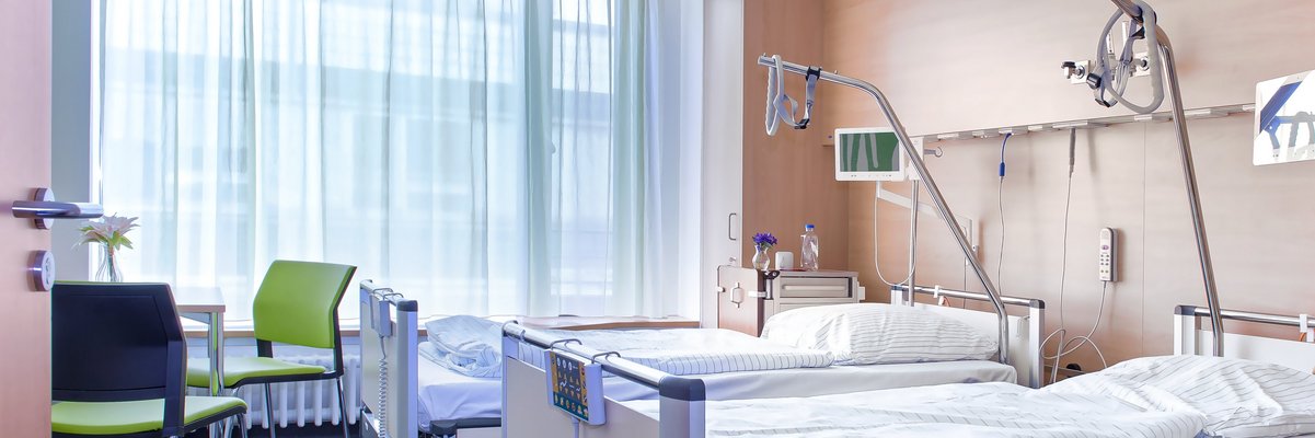 Patientenzimmer mit zwei Betten, Tisch und Beistelltischen