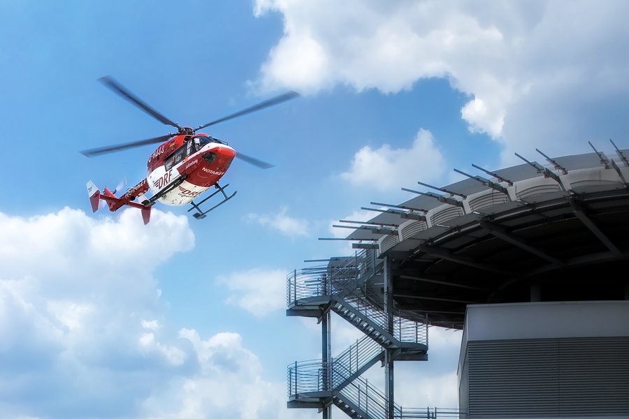 Ein rot-weißer Rettungshubschrauber fliegt in der Nähe der Hubschrauberlandeplatt-form des Universitätsklinikums Halle (Saale). Von der Plattform führt eine Treppe nach unten.  Ein rot-weißer Rettungshubschrauber fliegt in der Nähe der Hubschrauberlandeplatt-form des Universitätsklinikums Halle (Saale). Von der Plattform führt eine Treppe nach unten.