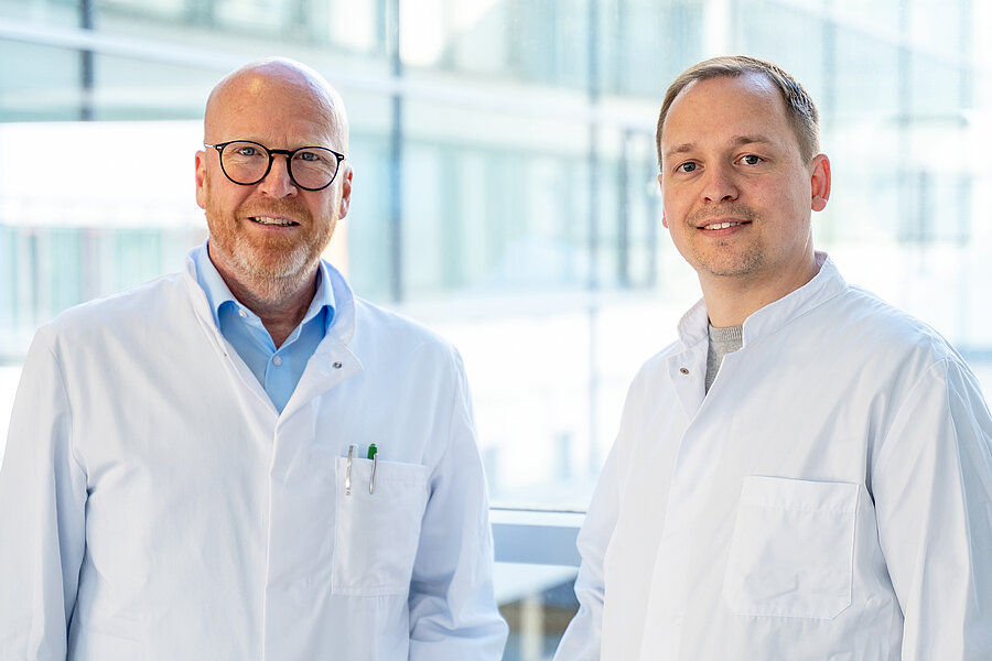 Zwei Männer stehen in einem Gang des Universitätsklinikums Halle (Saale) und schauen in die Kamera. Beide tragen Arztkittel.  Zwei Männer stehen in einem Gang des Universitätsklinikums Halle (Saale) und schauen in die Kamera. Beide tragen Arztkittel.