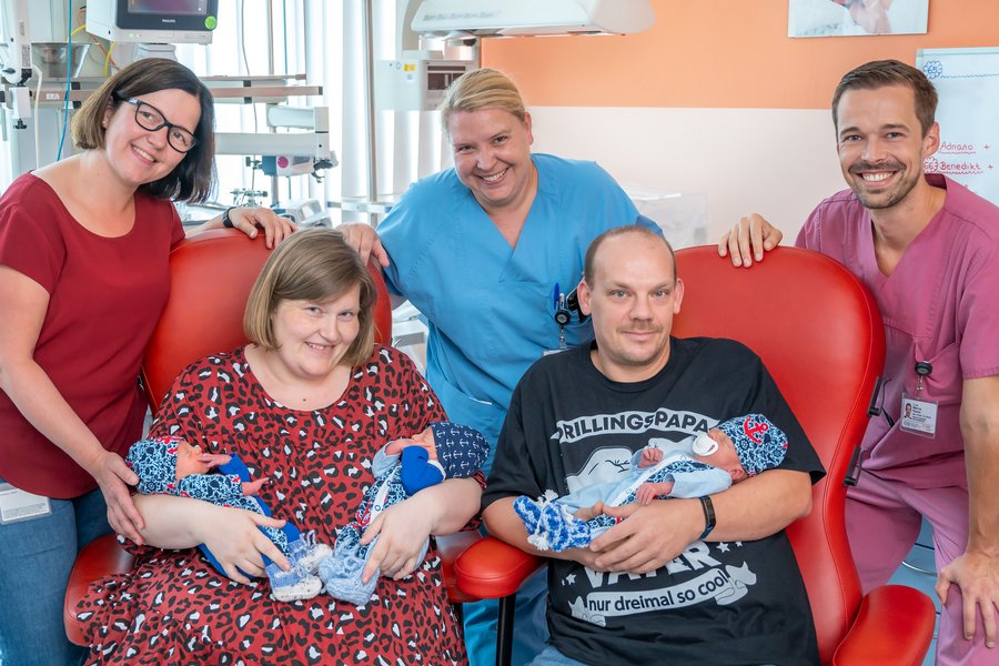 Die Eltern sitzen auf Stühlen und halten ihre Drillinge im Arm. Nicole Rostalski, Sandy Reinhardt und Dr. Marcus Riemer stehen dahinter.  Die Eltern sitzen auf Stühlen und halten ihre Drillinge im Arm. Nicole Rostalski, Sandy Reinhardt und Dr. Marcus Riemer stehen dahinter.