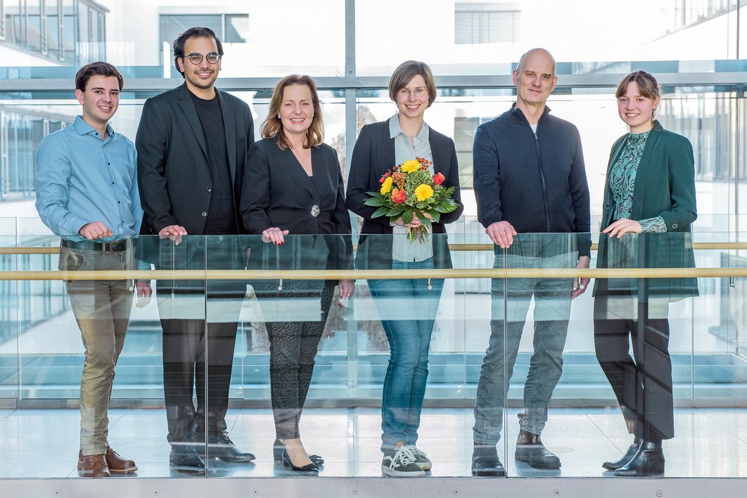 Sechs Personen stehen in einem lichtdurchfluteten Korridor. Eine Person in der Mitte hält einen Blumenstrauß. Sie ist die Lehrpreisträgerin aus der Zahnmedizin. 